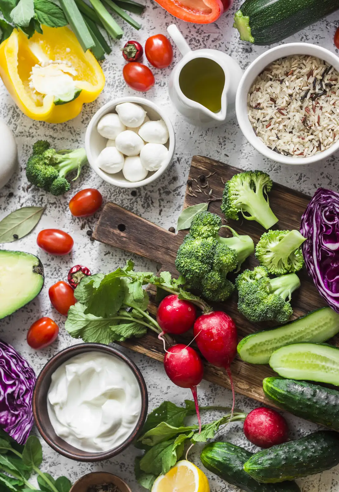 Fresh vegetables, herbs, wild rice and cheeses laid out on a wooden prep board